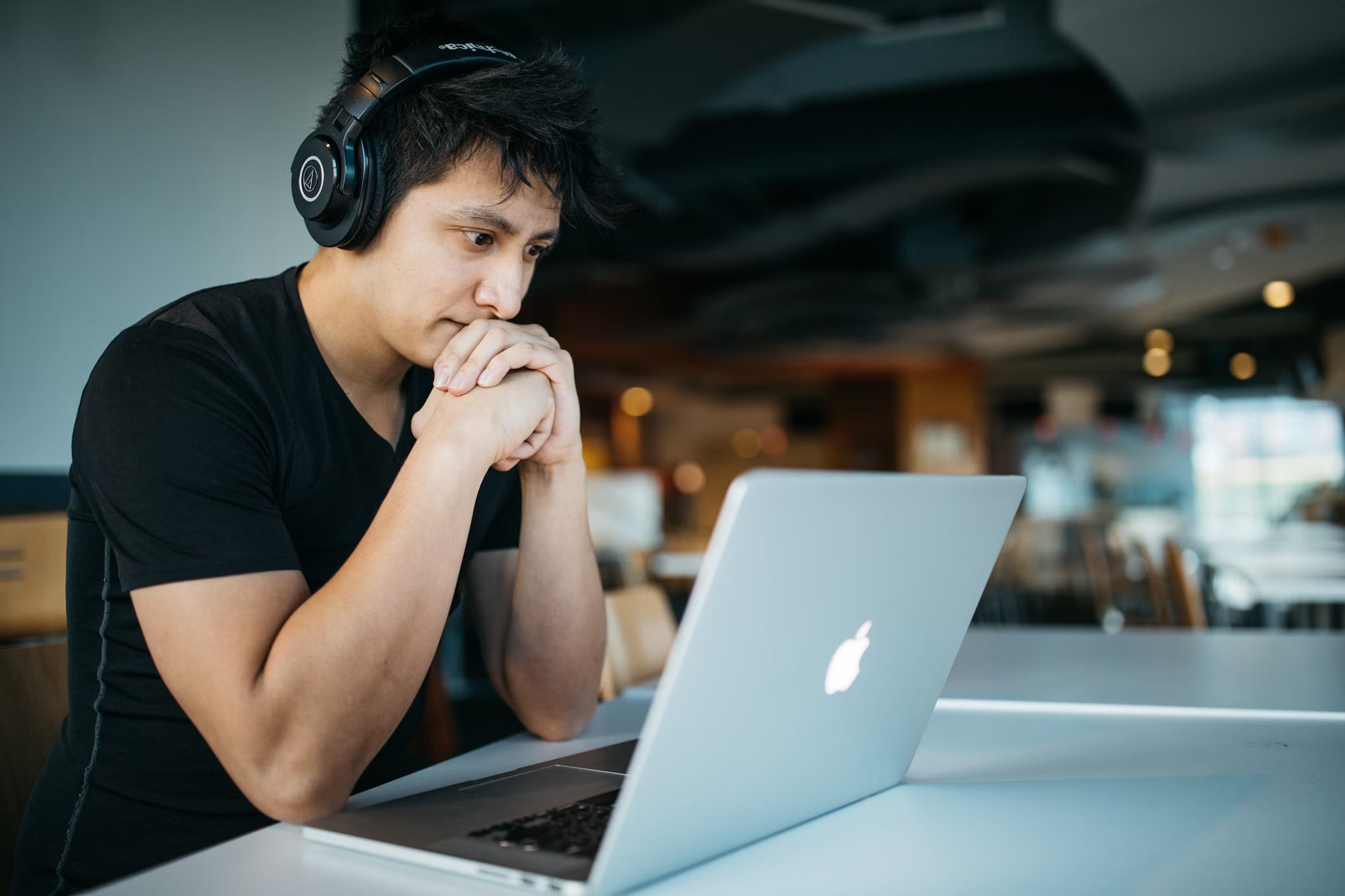 homem usando fones de ouvido enquanto esta sentado em uma cadeira em frente ao MacBook